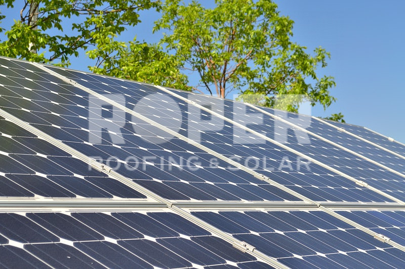 Solar panels on residential roof with green trees and blue sky background
