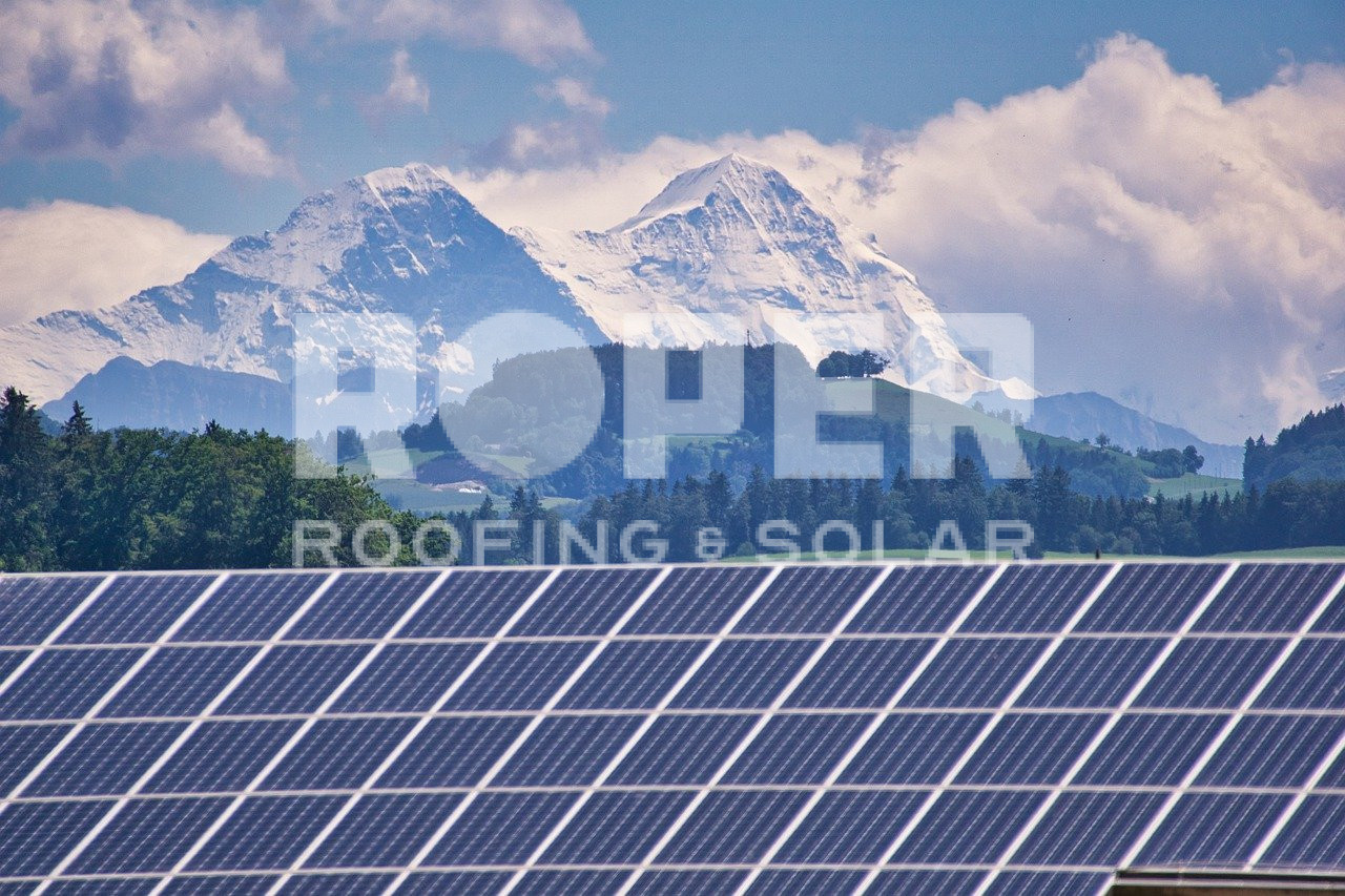 Solar panel farm with snow-capped mountains and cloudy sky in background