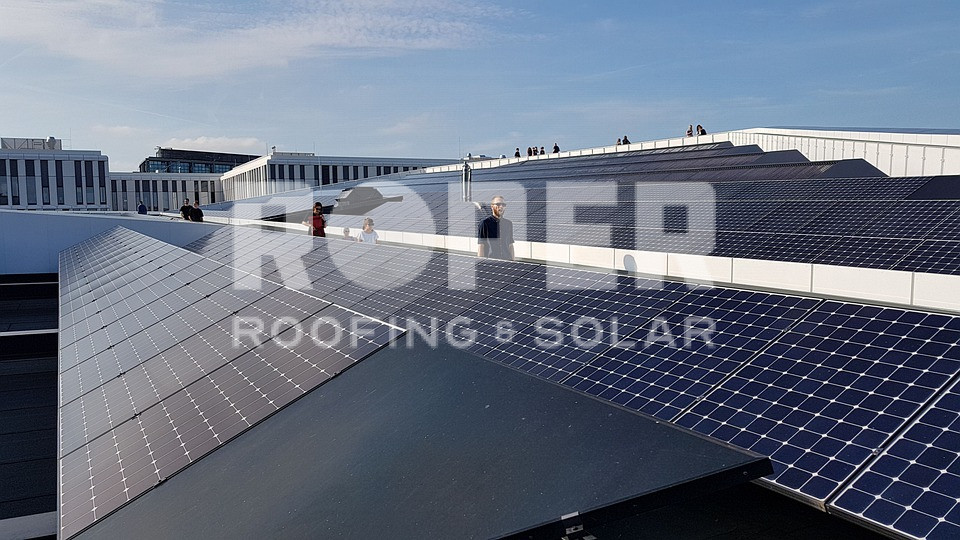 Large solar panel installation on modern building rooftop with people walking
