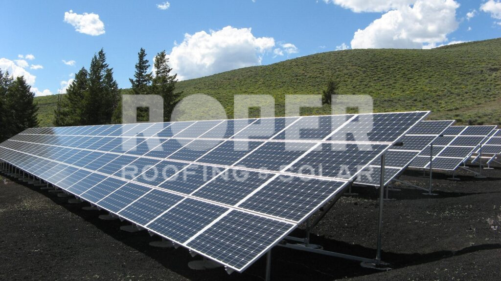 Solar panel array installation on rural hillside with green mountains and blue sky