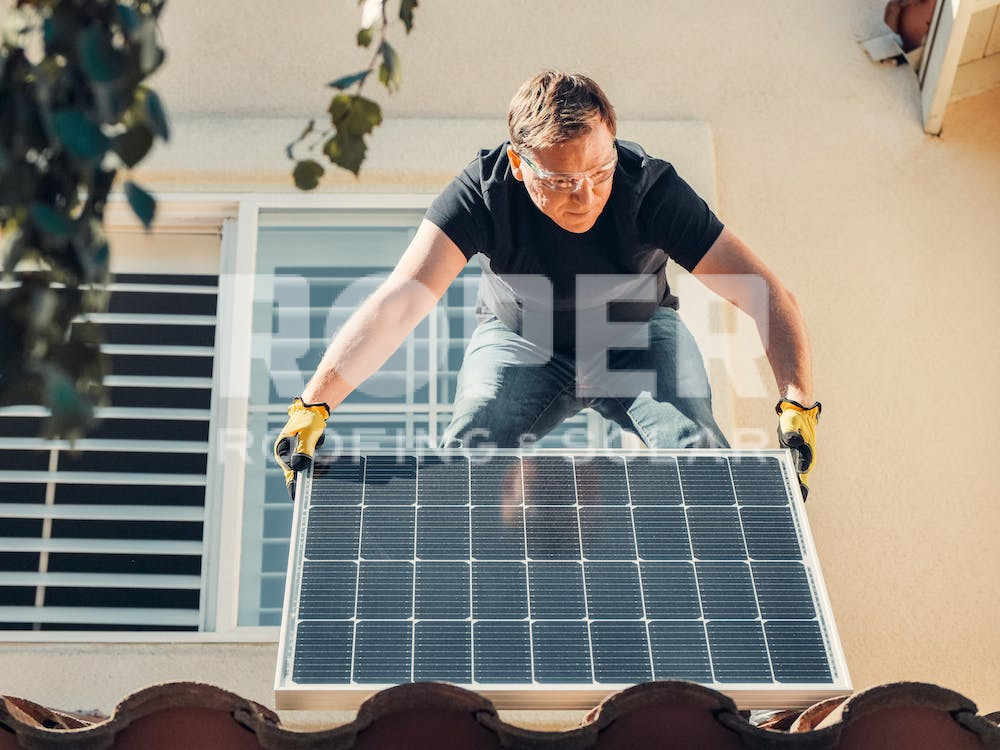 Worker installing solar panel on residential roof wearing safety glasses and gloves