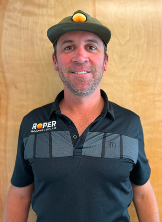 Smiling man in dark polo shirt and green cap with logo standing against wood wall